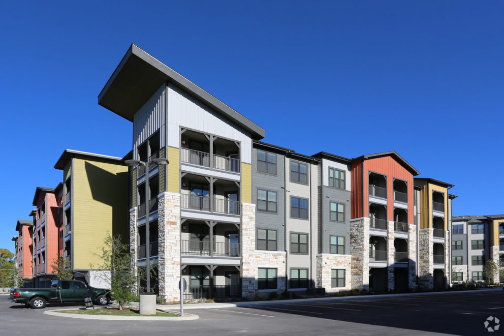 Multi-story apartment building exterior with colorful siding, stone accents, and balconies under a clear blue sky