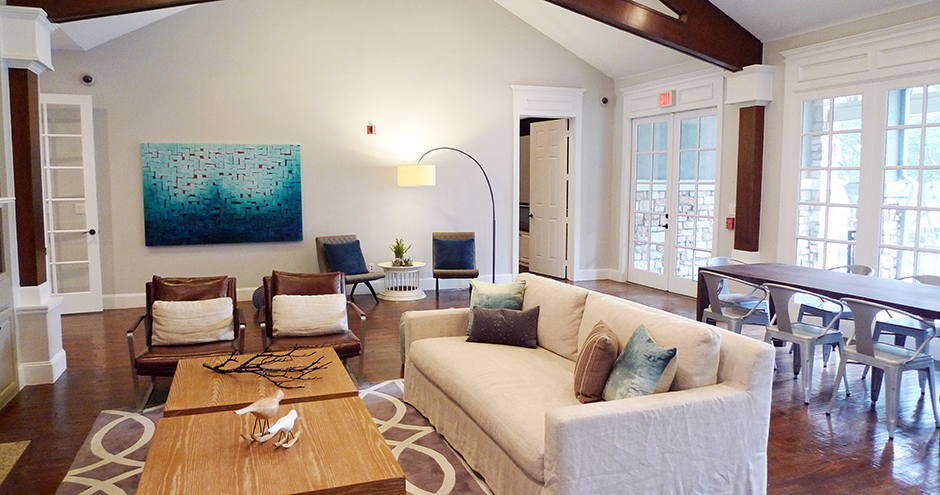 A bright, modern living room with a beige sofa, leather chairs, wooden coffee table, and blue abstract artwork on the wall